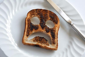 a burnt slice of toast with eyes and a frown cut out of it.